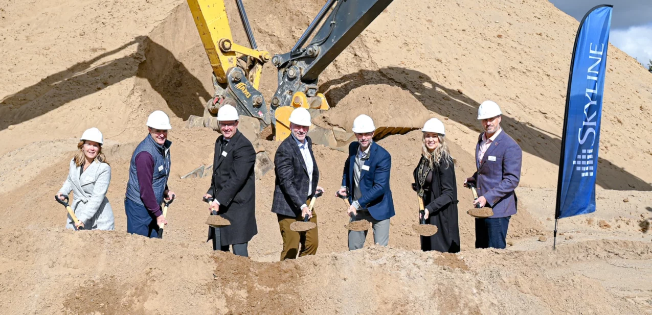 Smiling people with groundbreaking shovels and hard hats at a construction site.