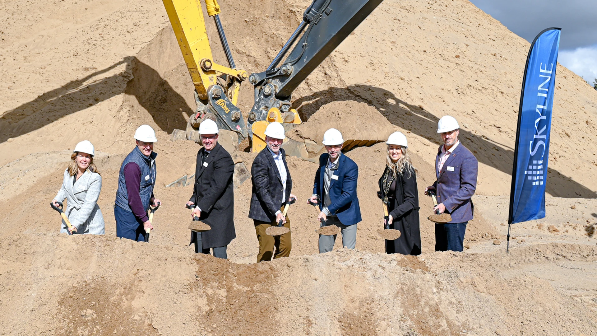 Smiling people with groundbreaking shovels and hard hats at a construction site.