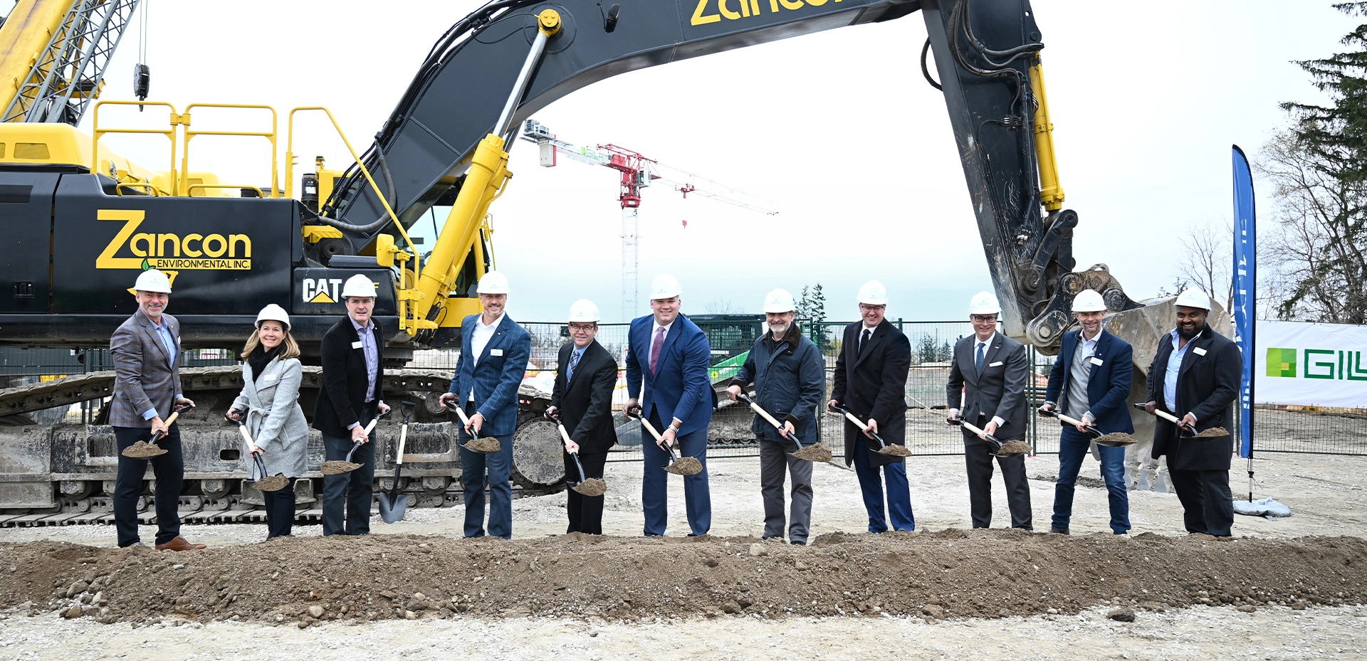 Smiling people with groundbreaking shovels and hard hats at a construction site.